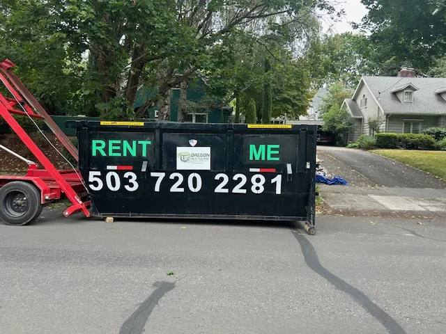Oregon Recycling roll-off dumpster beside its red delivery trailer on a residential street.