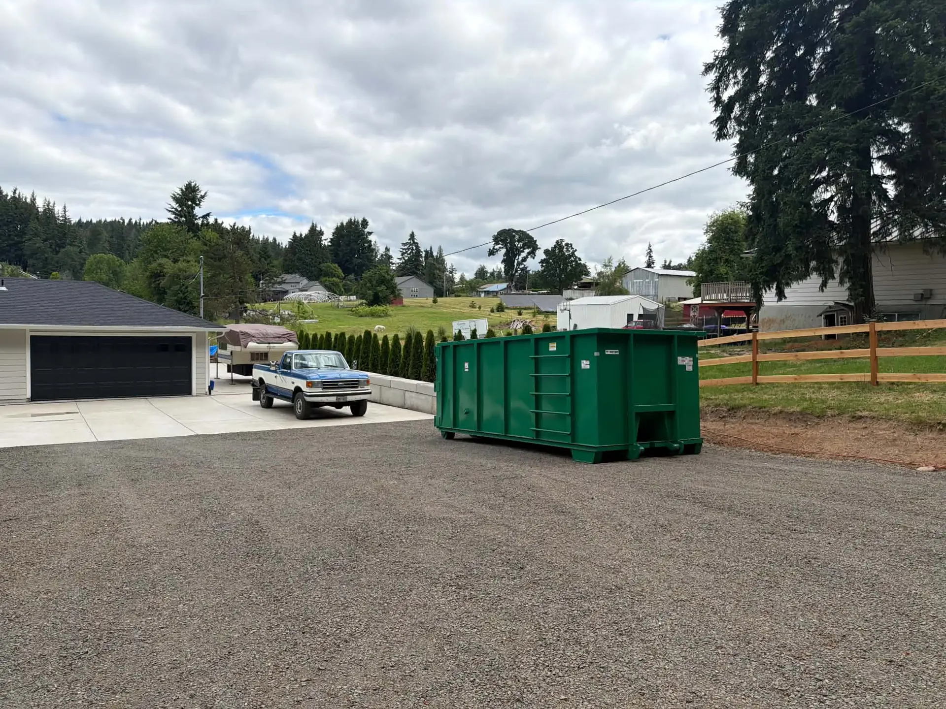 Green Oregon Recycling roll-off dumpster on a paved area beside a garage.