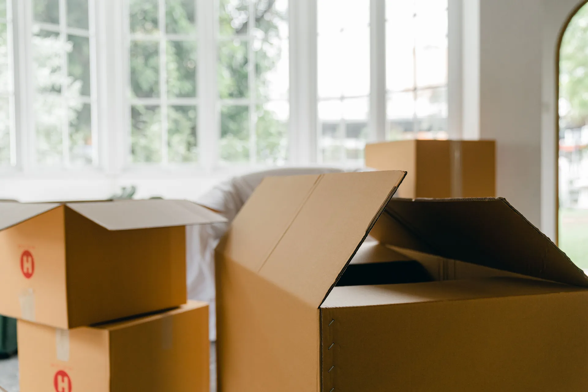 Open cardboard boxes beside covered furniture in a sunlit room.