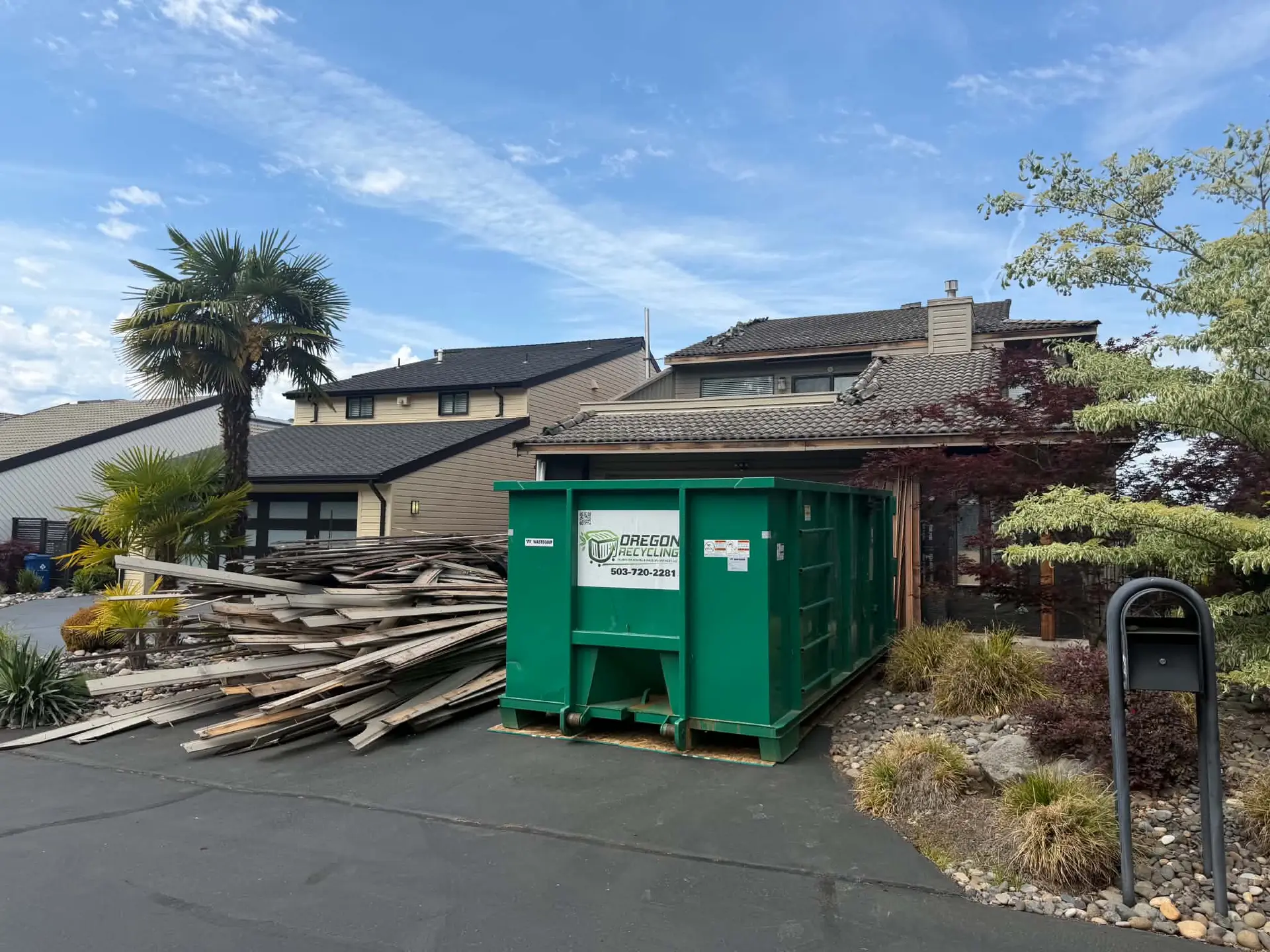 Oregon Recycling dumpster beside stacked wood debris outside a home.