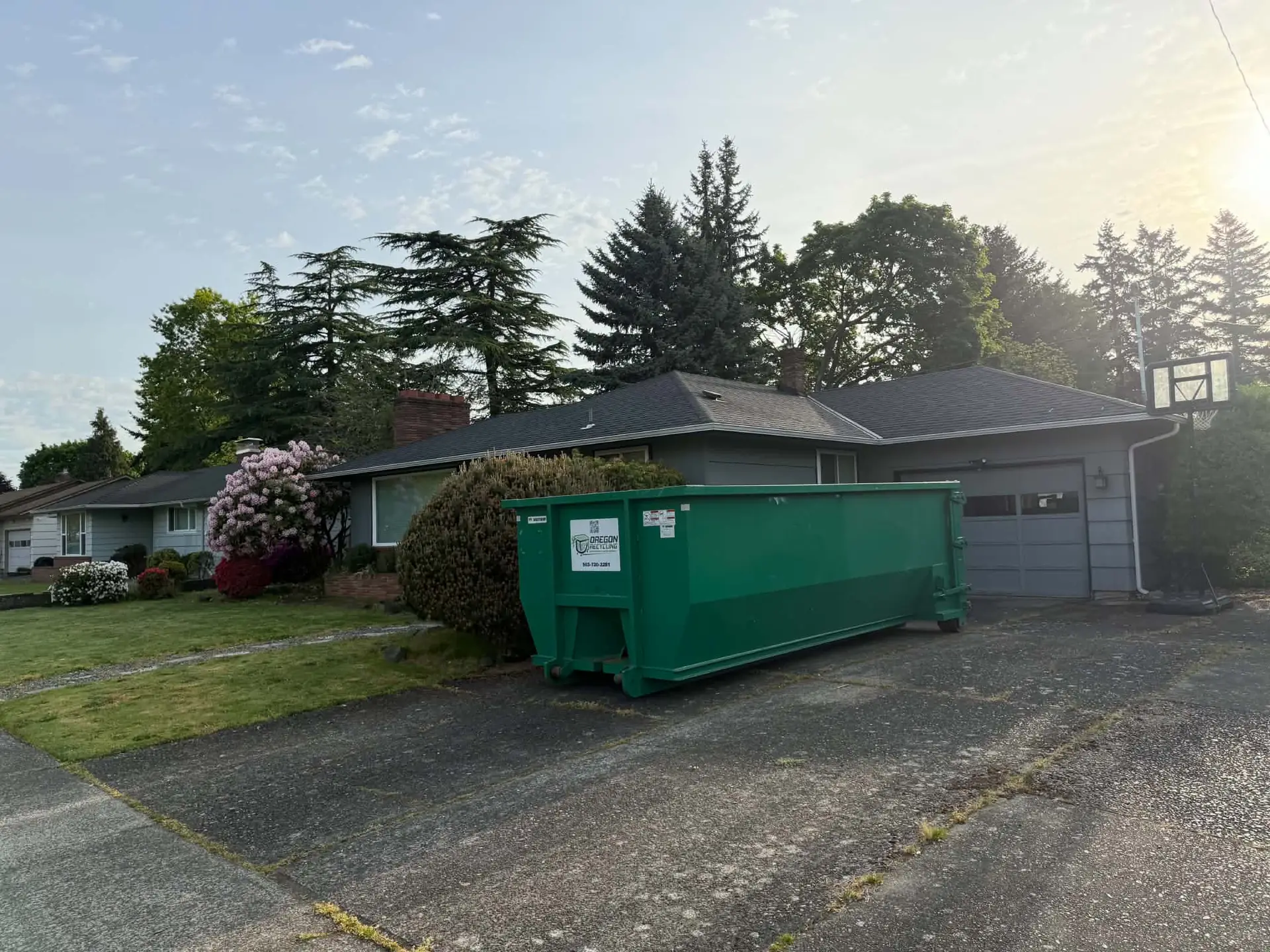 Green Oregon Recycling dumpster on a driveway in front of a home and garage.