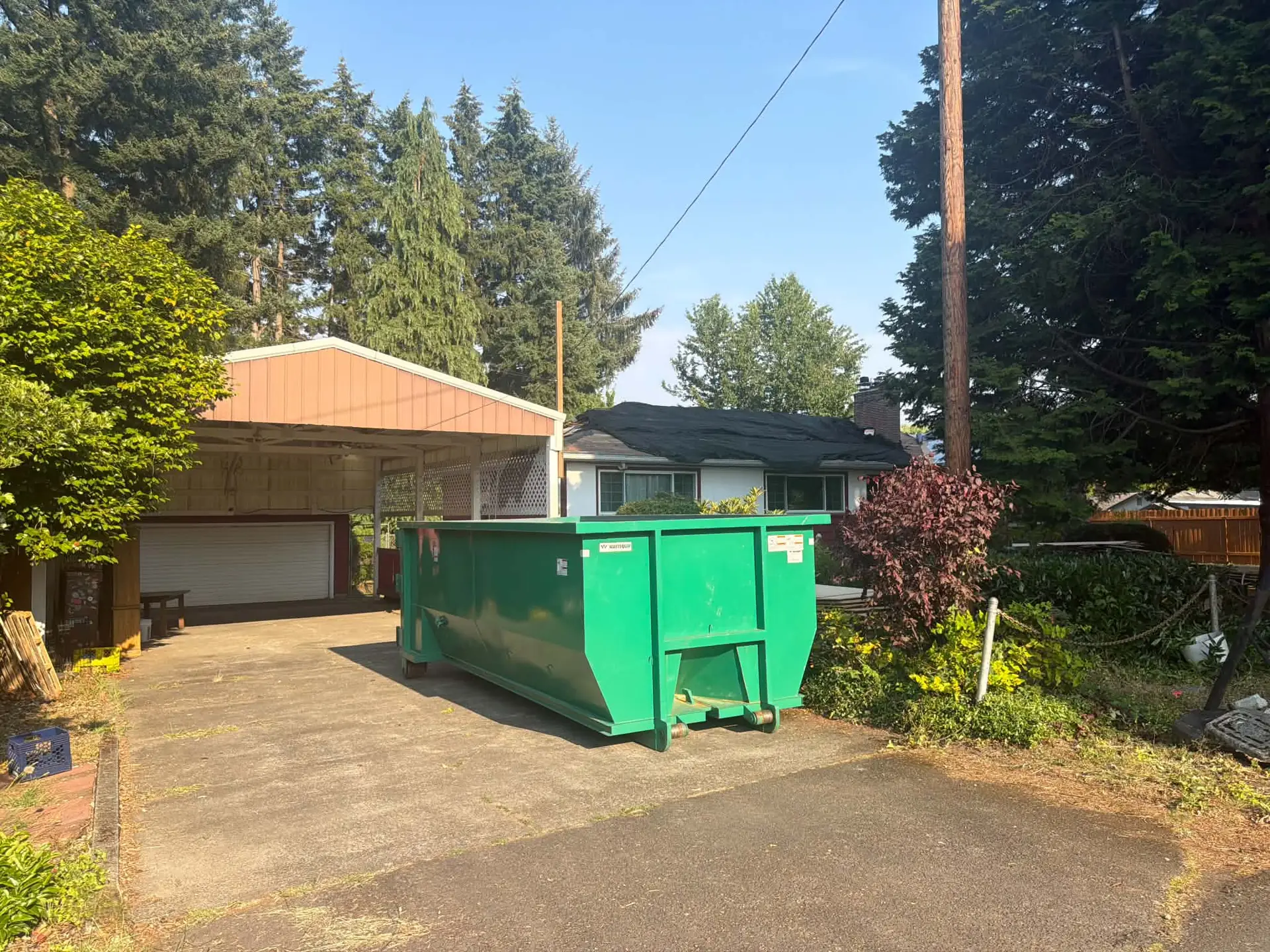 Green Oregon Recycling dumpster set in a sunny driveway beside a garage.