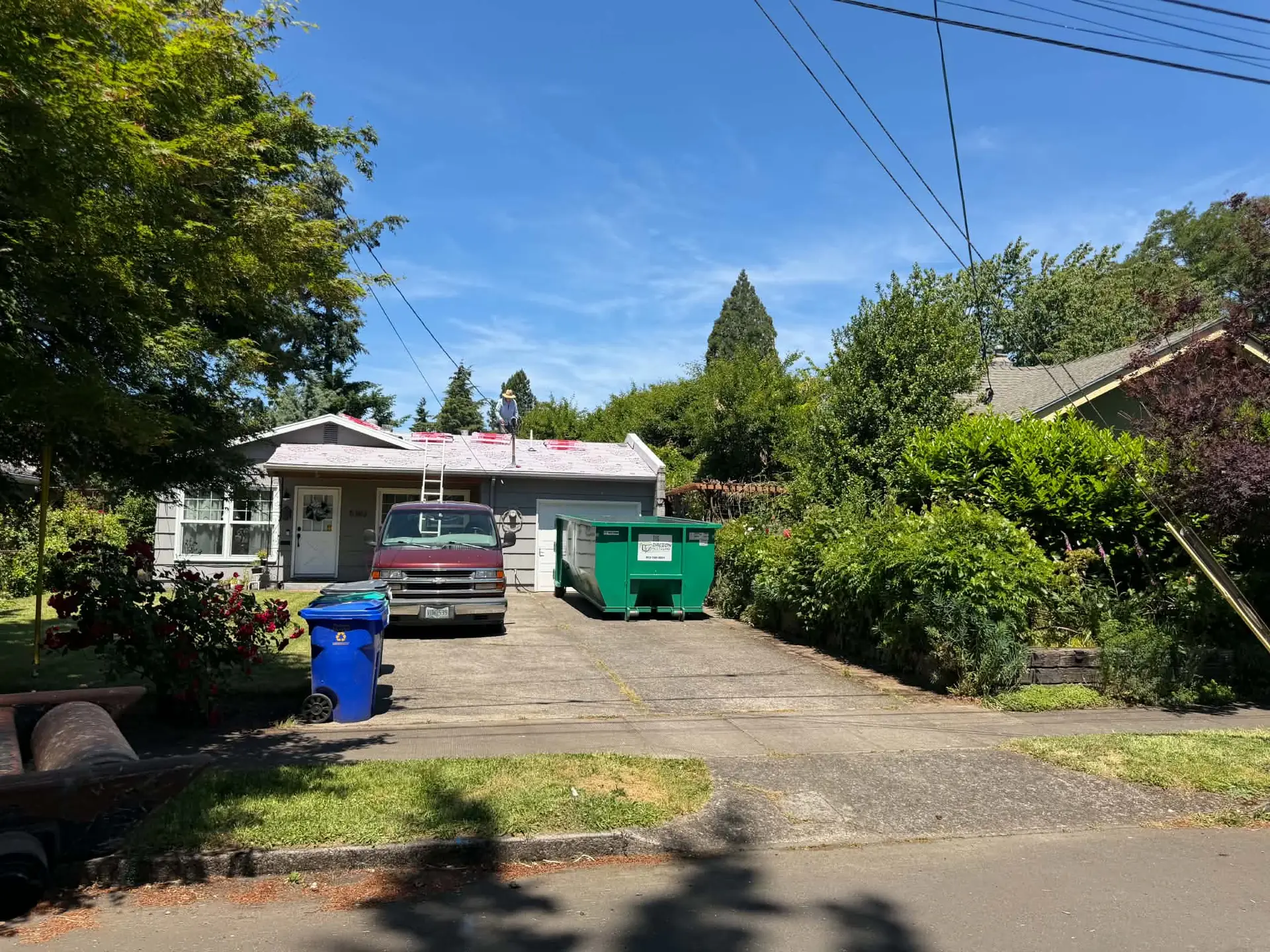 Green Oregon Recycling dumpster in a driveway beside a home with roof work underway.