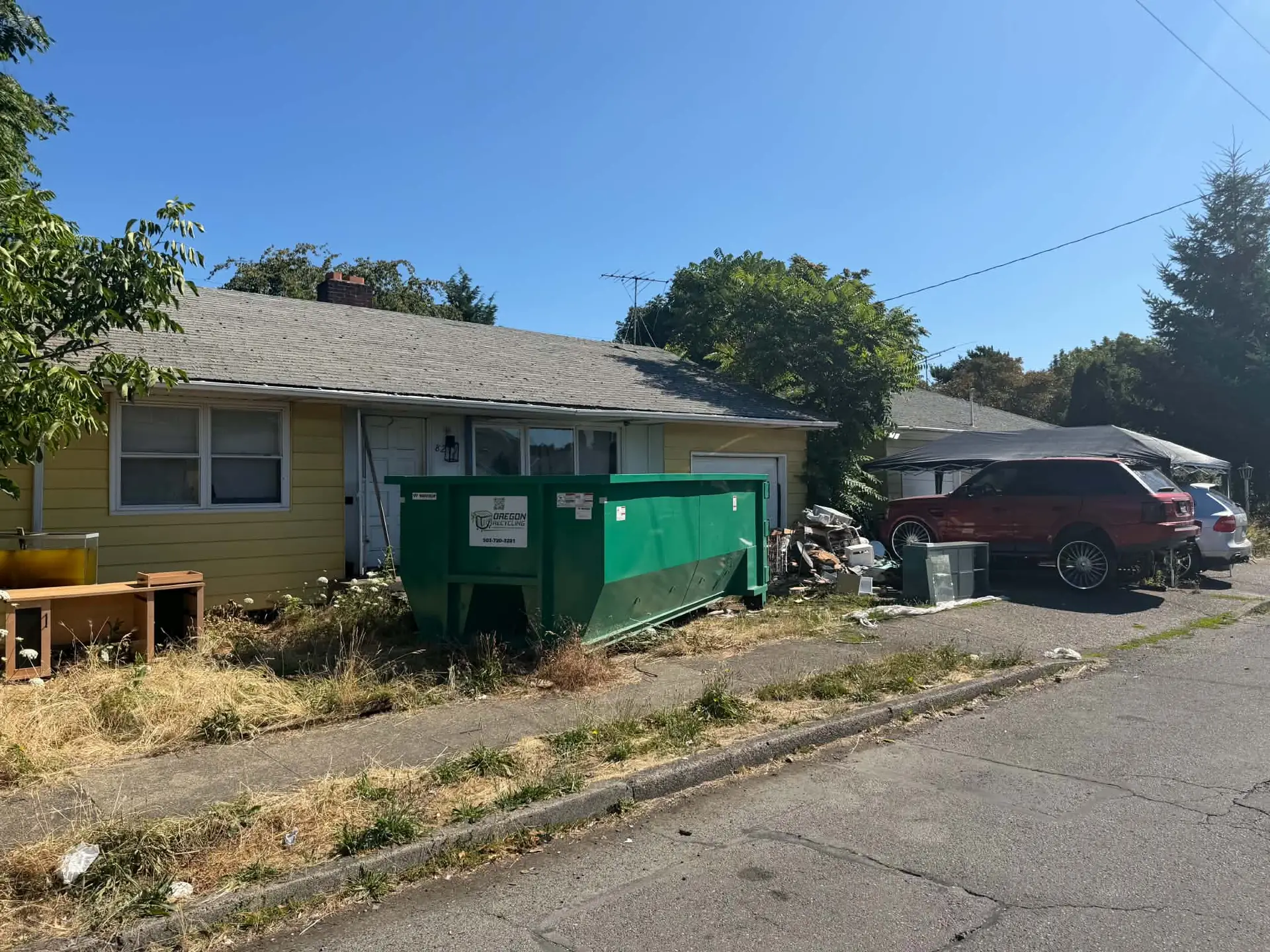 Oregon Recycling dumpster beside household items at a residential cleanup.