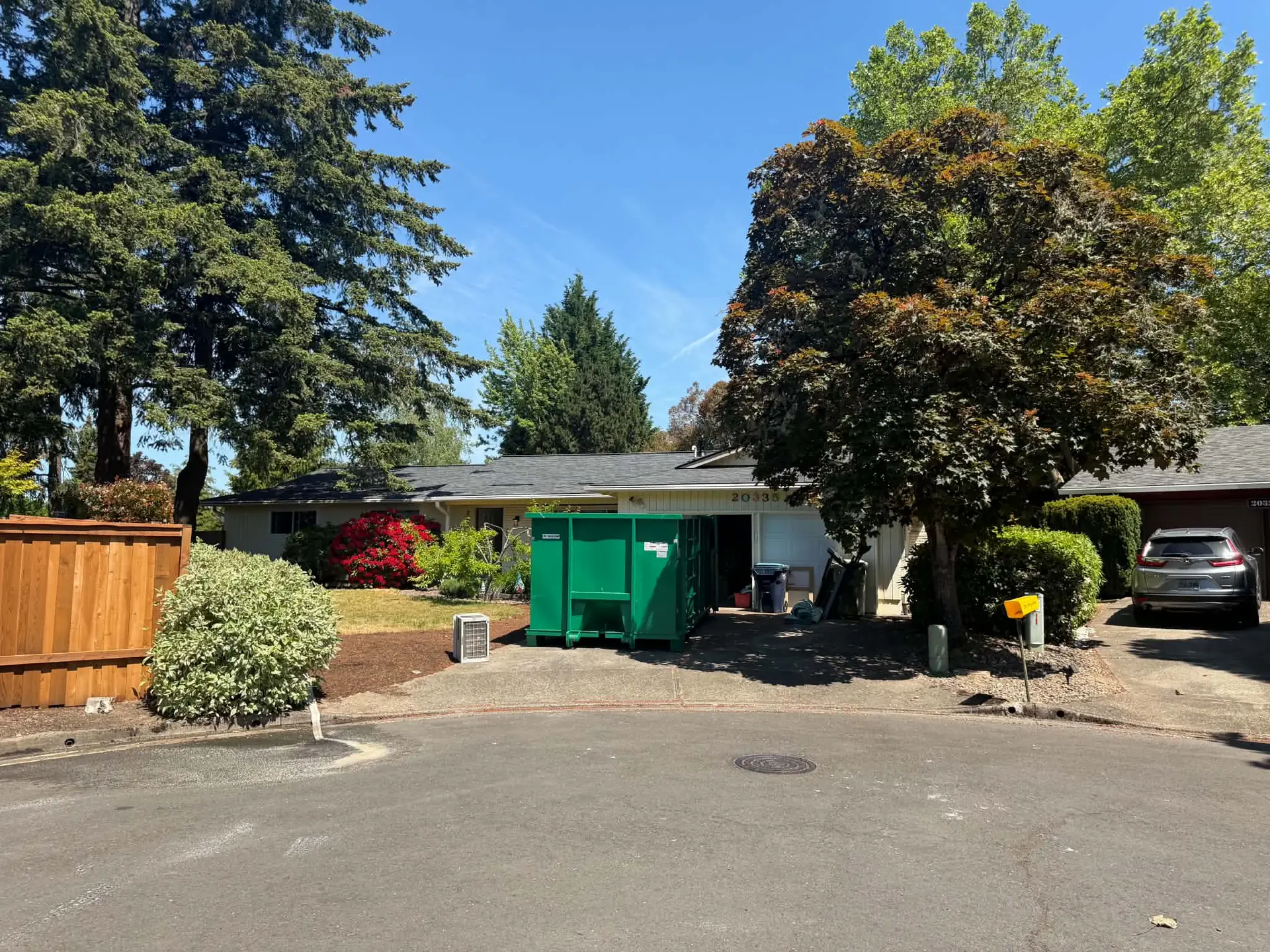 Oregon Recycling dumpster in a residential driveway beneath mature trees.