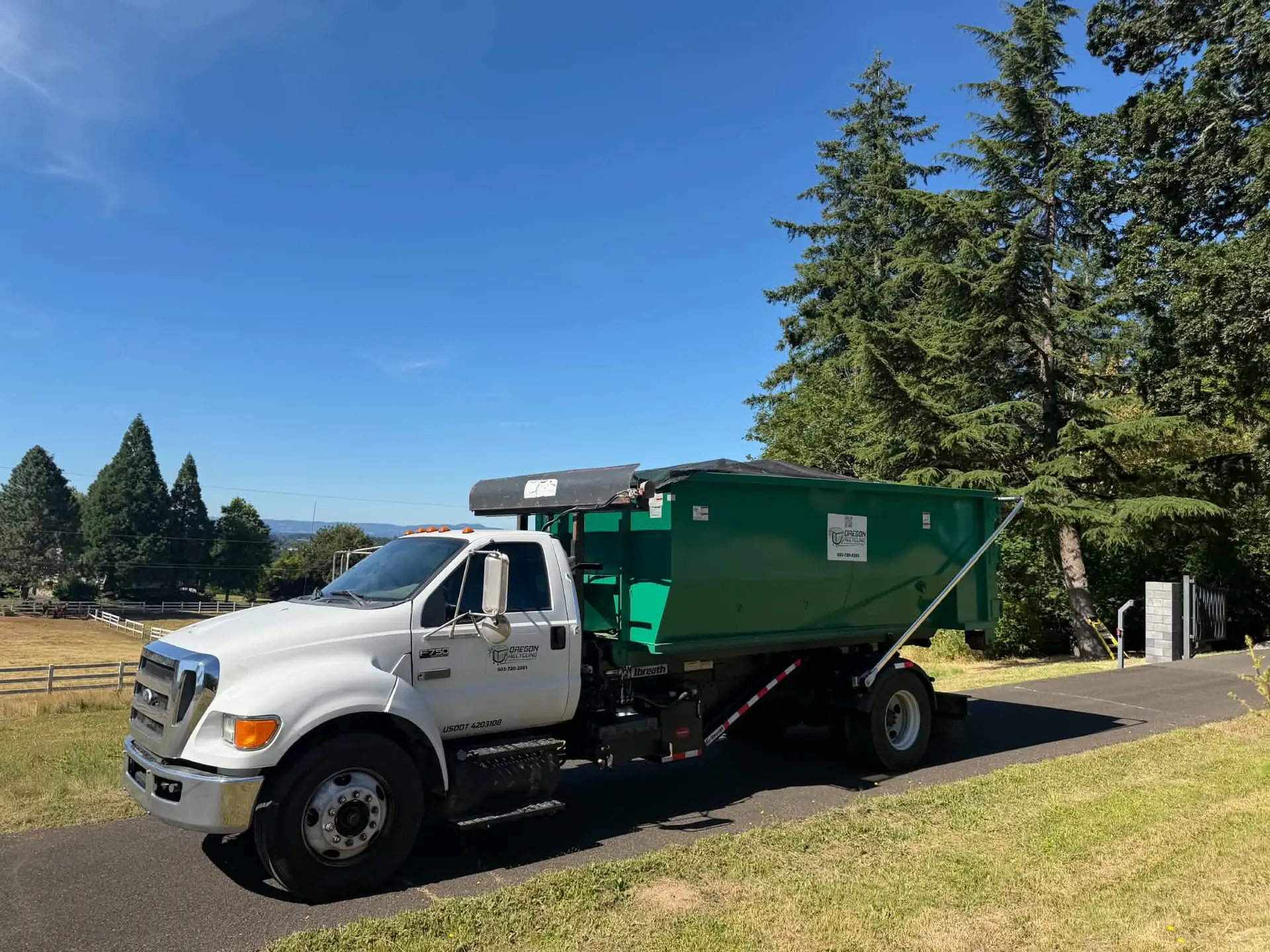 White Oregon Recycling truck carrying a green roll-off container.