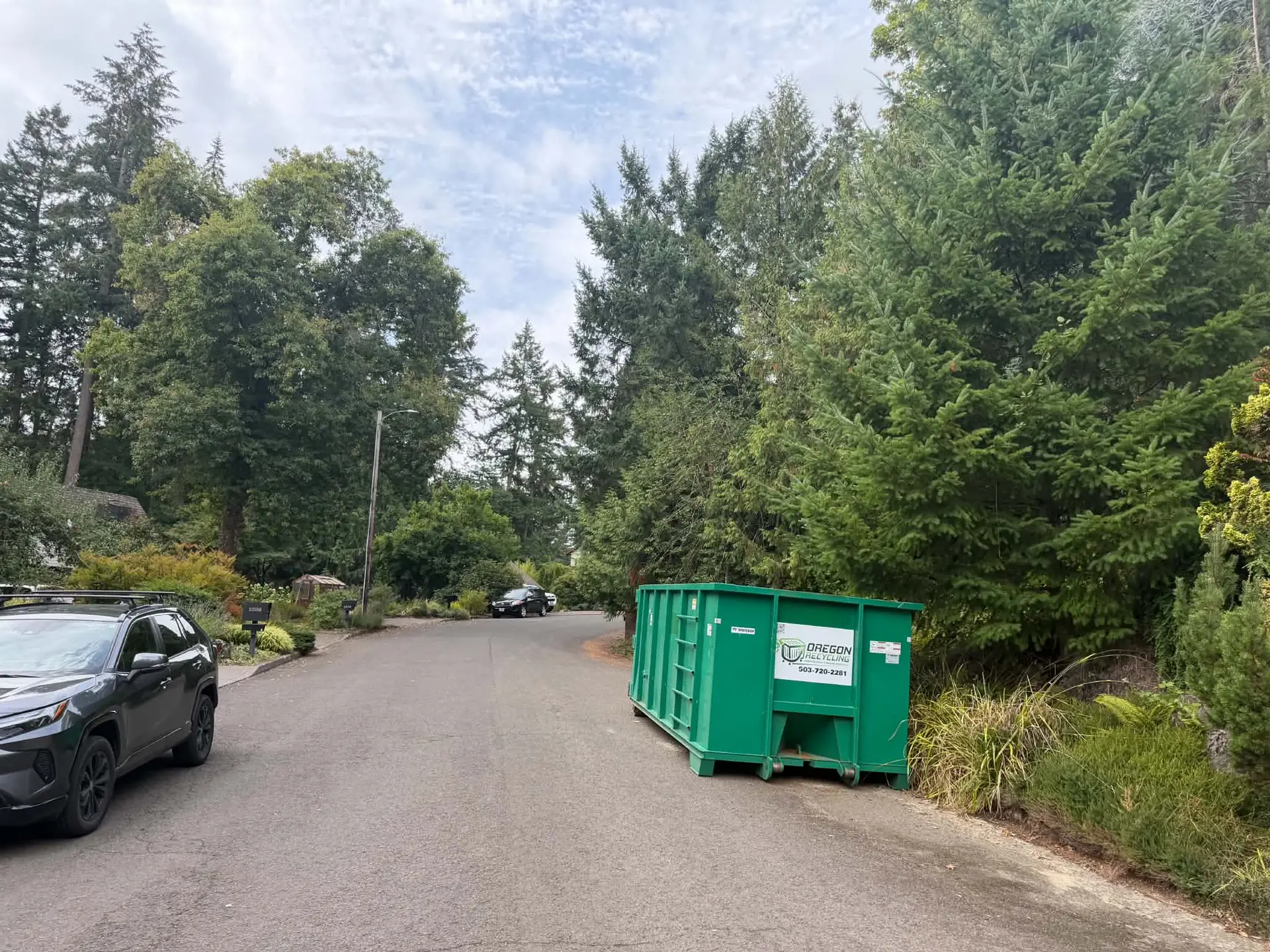 Oregon Recycling dumpster beside a tree-lined residential road.